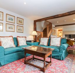 A living room with two teal sofas a wooden coffee table framed pictures on the wall and exposed wooden beams at Glanville House in Mevagissey