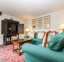 A sitting room with teal sofas a wooden coffee table a dark wooden cabinet with a television and framed pictures on the wall at Glanville House in Mevagissey