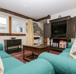 A living room with turquoise sofas a wooden coffee table a TV in a wooden cabinet and exposed stone and wooden beams at Glanville House in Mevagissey