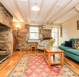 A living room with stone walls a wood burning stove a teal sofa an armchair and a wooden coffee table with flowers at Gurnard's Cottage in St Ives