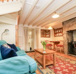 A living room with a blue sofa a wooden coffee table with flowers a stone fireplace and a dining table with chairs at Gurnard's Cottage in St Ives