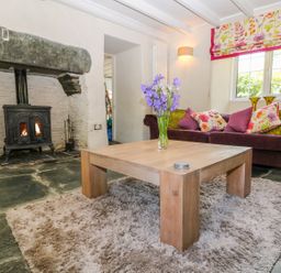 A living room with a wood stove fireplace wooden coffee table with flowers and a sofa with cushions at Parwin Tintagel