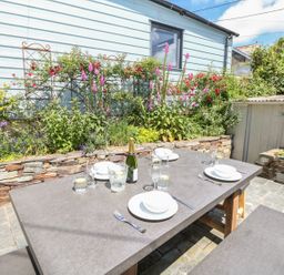 An outdoor dining area with a table set with plates glasses and a bottle in a garden at Parwin in Tintagel