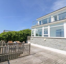 A balcony with wooden decking and outdoor dining set attached to a building with large windows at St Ives View in Porthtowan