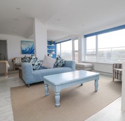 A living room with a blue sofa and table a striped armchair and large windows at St Ives View in Porthtowan