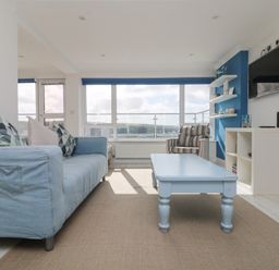 A living room with a blue sofa striped armchair blue coffee table wall-mounted tv and large windows at St Ives View in Porthtowan