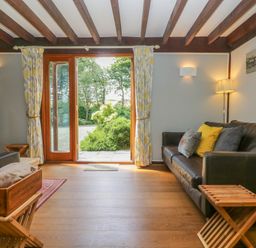 A living room with a brown leather sofa wooden beams and glass doors opening to a garden at Oaklands Near Boscastle