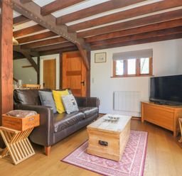 A living room with a leather sofa coffee table television and wooden beams at Oaklands Near Boscastle