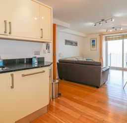 A kitchen and living area with cream cabinets brown sofa wooden floor and sliding glass door at Seasiders in Ilfracombe