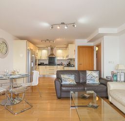An open living and kitchen area with a dining table and chairs a brown and a white sofa and a glass coffee table at Seasiders Ilfracombe