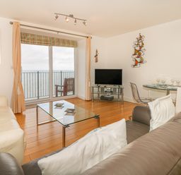 A living room with sofas glass coffee table dining table TV and balcony overlooking the sea at Seasiders Ilfracombe