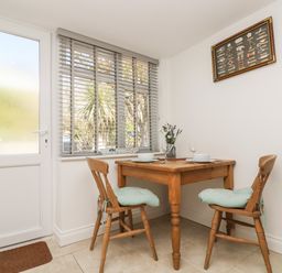 A small dining area with a wooden table and two chairs near a window and door at Seascape in Porthcurno