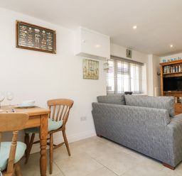 A dining table with chairs and a gray sofa next to a window in a living room at Seascape in Porthcurno