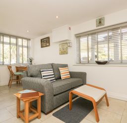 A living room with a gray sofa and striped cushions a small wooden table and a wooden stool with cushion at Seascape in Porthcurno