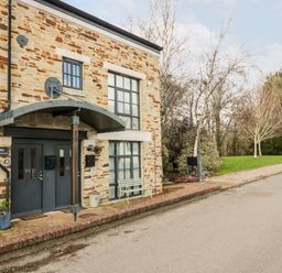 A two-door entrance with stone walls next to a paved road and trees at Riverview in Lostwithiel