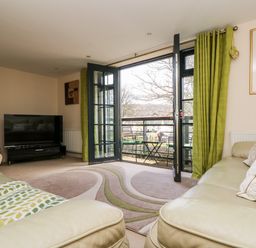 A living room with a television a beige sofa and open doors leading to a balcony at Riverview in Lostwithiel