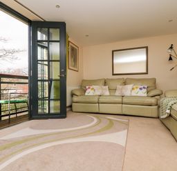 A living room with leather sofas rug and open door leading to a balcony at Riverview in Lostwithiel