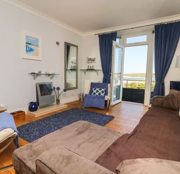 A living room with a brown sofa blue curtains and a balcony door open to a view at Tides in Padstow
