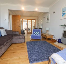 A living room with brown sofa a blue armchair a blue rug wooden floor and a wall-mounted television at Tides in Padstow