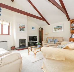 A living room with beige sofas, a glass coffee table, a wooden bookshelf, a television, and exposed wooden ceiling beams at Lookout in Falmouth