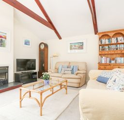 A living room with beige sofas glass coffee table wooden bookcase and television at Lookout in Falmouth