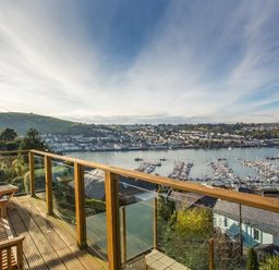 A wooden balcony with chairs overlooking a harbor with boats and houses at Totherside in Kingswear