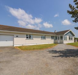 A single story house with garage and driveway surrounded by grass and trees at Seaport Lodge in Mawgan Porth