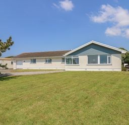 A single story house with a garage on a lawn with a paved driveway and a tree in the yard at Seaport Lodge in Mawgan Porth