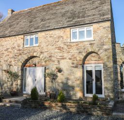 A stone house with arched doorways and windows with plants in pots outside at Lost Barn in Watergate Bay