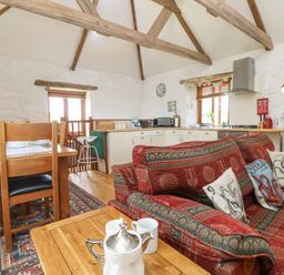 A kitchen and dining area with wooden beams on the ceiling and a red patterned couch at Courtyard in Nancegollan nr Porthleven