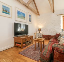 A living room with a patterned sofa wooden TV stand and framed pictures on the wall at Courtyard in Nancegollan nr Porthleven