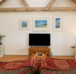 A living room with a television on a wooden stand and three framed pictures on the wall at Courtyard in Nancegollan nr Porthleven