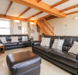 A living room with two black leather sofas cushions a wooden side table and exposed wooden beams at Boslow in St Just