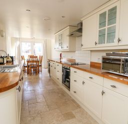 A kitchen with wooden countertops white cabinets a stainless steel microwave a sink and a dining table with chairs at Boslow in St Just