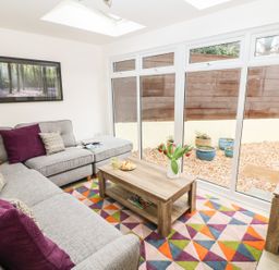 A living room with a grey sectional sofa and colorful cushions a wooden coffee table with flowers next to large windows at Higher Kernick Stable in Helland near Blisland