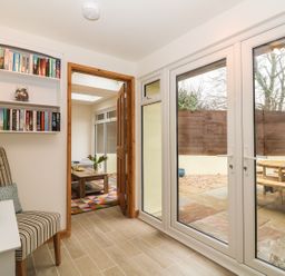 A room with a striped chair a small table with green apples shelves with books a door leading to another room and glass doors opening to a patio at Higher Kernick Stable Helland near Blisland