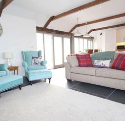 A living room with blue armchairs a beige sofa and a large clock on the wall at The Old Dairy in Padstow