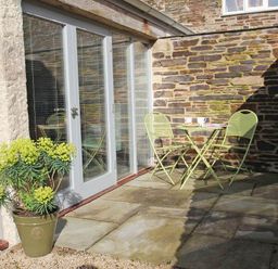 A small patio with a green potted plant and green metal table and chairs outside a stone wall building at The Old Dairy in Padstow