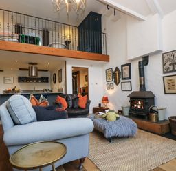 A living room with a wood stove a gray armchair a furcovered ottoman and framed pictures on the wall at Hideaway in Watergate Bay