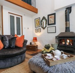 A living room with a fireplace a round dark sofa with orange and grey cushions and a tea set on a tray on a furry ottoman at Hideaway in Watergate Bay
