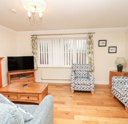 A living room with patterned armchairs wooden coffee table television and fireplace at Fairways in Woolacombe