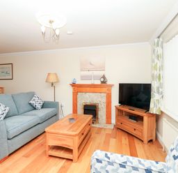 A living room with a blue sofa two patterned cushions wooden coffee table wooden cabinet with a television and a fireplace at Fairways in Woolacombe