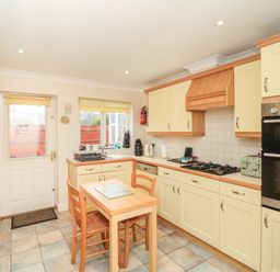 A kitchen with a small wooden table and two chairs a sink a window a door oven and stovetop at Fairways in Woolacombe