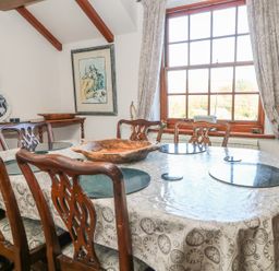 A dining room with a wooden table and chairs and a large window with curtains at Mengarth in Cadgwith