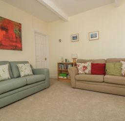 A living room with two sofas, cushions, a small bookshelf with books and a lamp, and paintings on the walls at Gannet Watch in Coverack