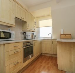 A kitchen with wooden cabinets a microwave oven a stove a kettle and a window with a blind at Gannet Watch in Coverack