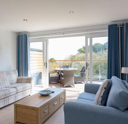 A living room with two sofas a wooden coffee table a wall-mounted TV and a balcony with outdoor furniture at Bayview in Brixham