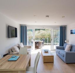 A living room with two sofas a wooden coffee table and dining table near glass doors at Bayview in Brixham