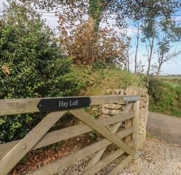 A wooden gate with a sign saying Hay Loft beside a gravel driveway and greenery at Hay Loft in Bolenowe Nr Portreath