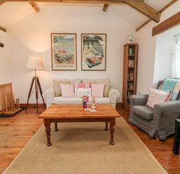 A living room with a beige sofa and gray armchair a wooden coffee table and framed posters on the wall at Hay Loft Bolenowe Nr Portreath